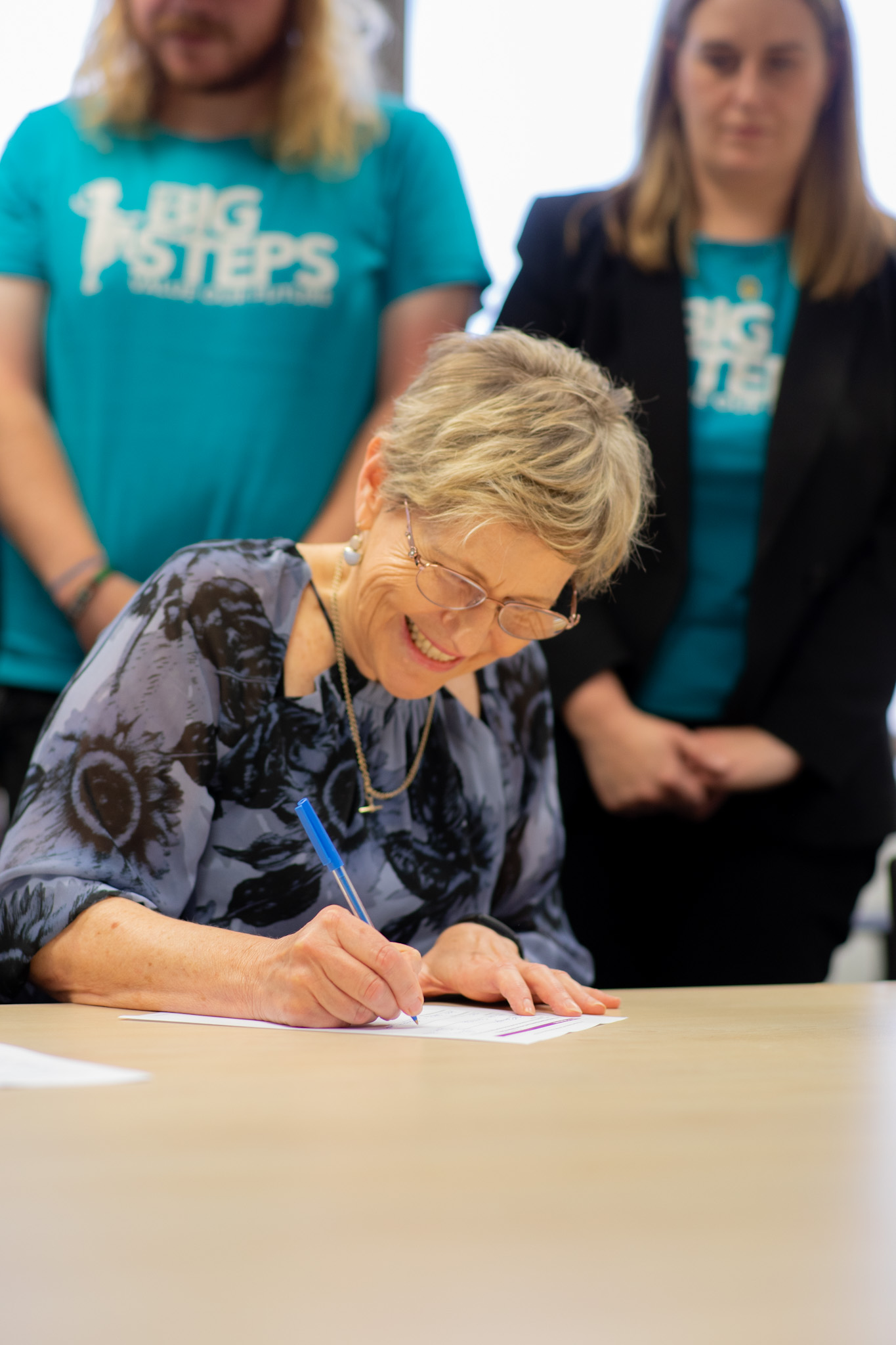 Smiling woman signing agreement with Big Steps professionals are in the background