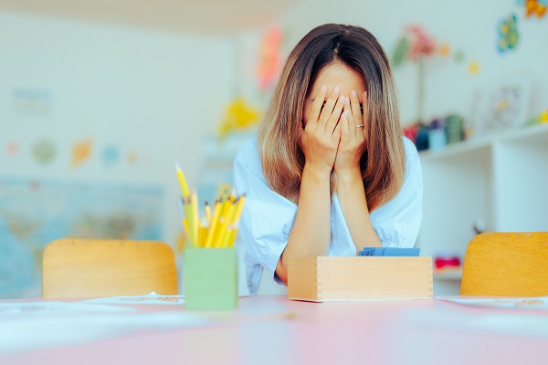 Educator sitting in a child care setting with hands covering their face in distress