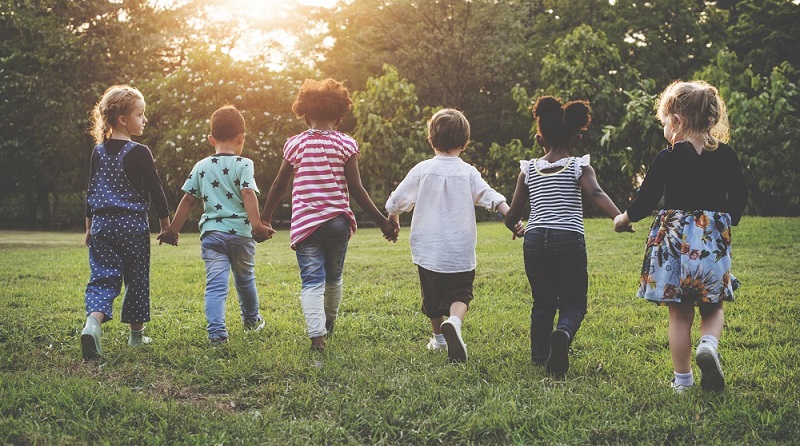 Children in a row holding hands and running through a park